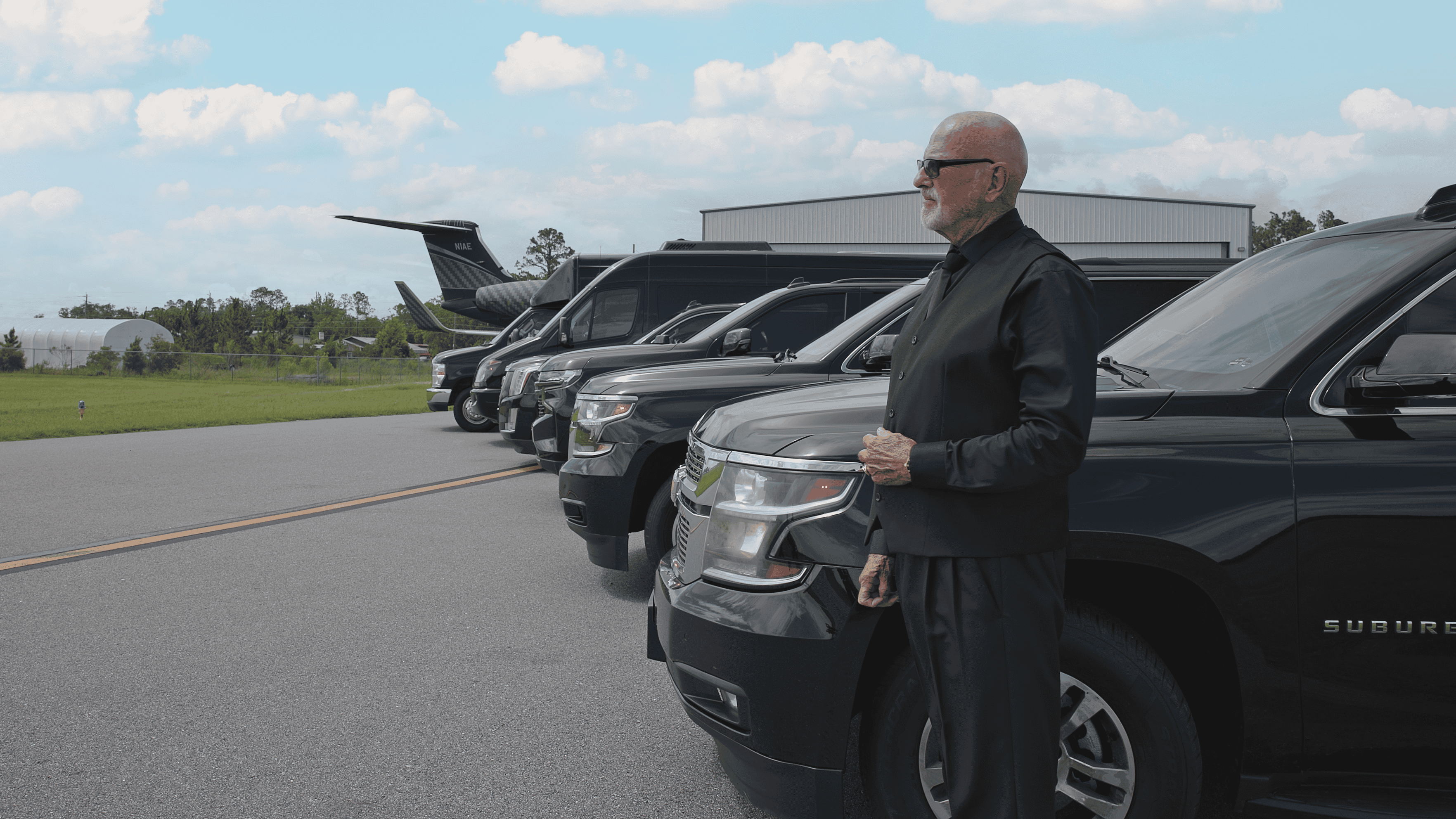 Professional chauffeur standing beside a lineup of luxury SUVs and executive vehicles at Sheltair Aviation in Ocala, providing private airport transportation.