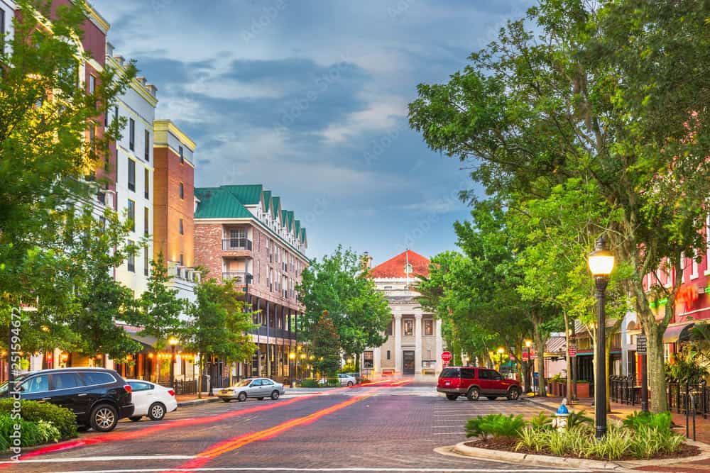 Downtown Gainesville streetscape featuring historic architecture, tree-lined sidewalks, and the Alachua County Courthouse in the distance.