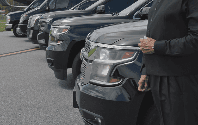 Professional FTS Limousine chauffeur standing beside a lineup of luxury SUVs, executive Sprinter vans, and shuttle buses, representing premium chauffeur-driven transportation throughout Gainesville, Jacksonville, Ocala, St. Augustine, and North Florida.