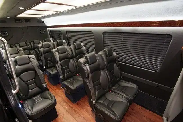 Interior of a 14-passenger executive Mercedes Sprinter with stadium seating, high-back captain chairs, woodgrain flooring, and perimeter lighting – luxury limousine service in Florida