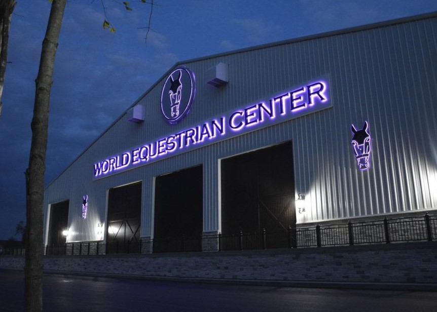 World Equestrian Center stable in Ocala Florida with large roll-up doors and illuminated blue signage.