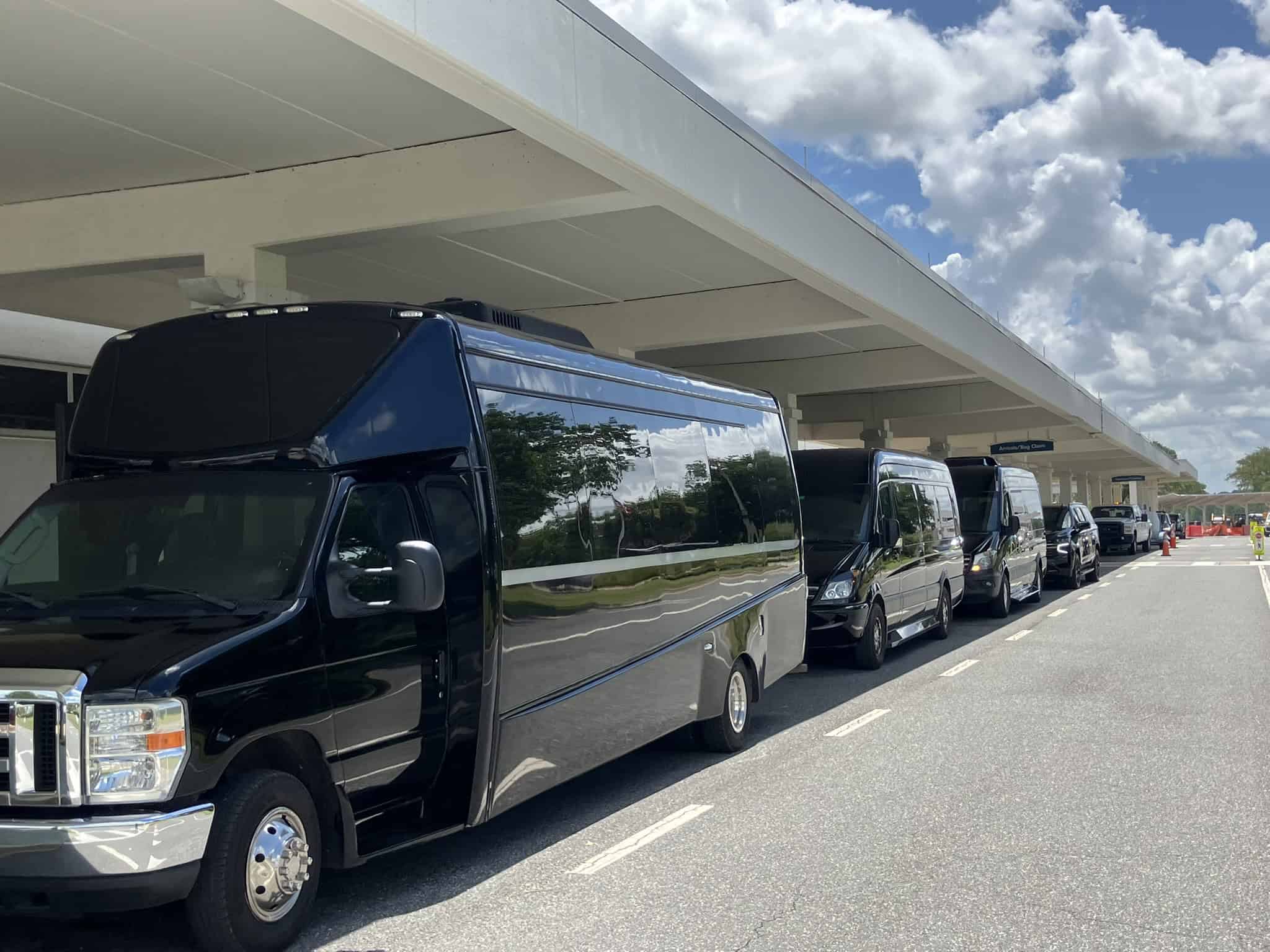 FTS Limousine executive shuttle bus, two Mercedes Sprinters, and a luxury SUV staged outside the arrivals and baggage claim area at Gainesville Regional Airport in Gainesville, Florida.