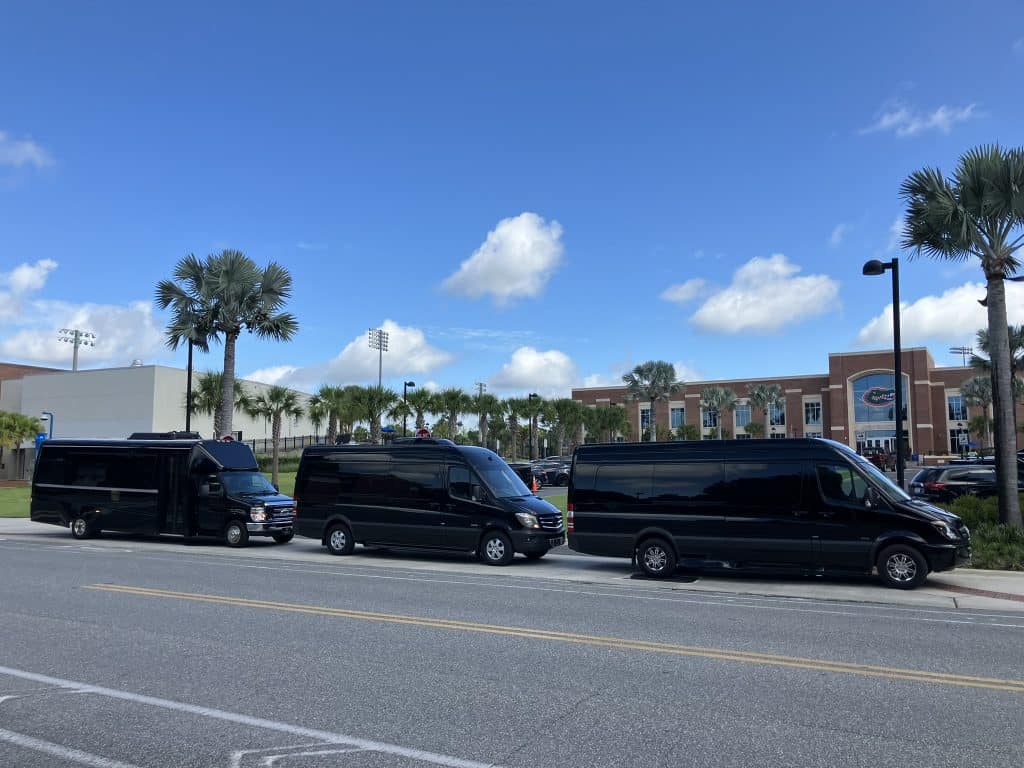Luxury Mercedes Sprinter vans and executive shuttle bus staged outside the University of Florida Heavener Football Facility in Gainesville, FL for game day group transportation.
