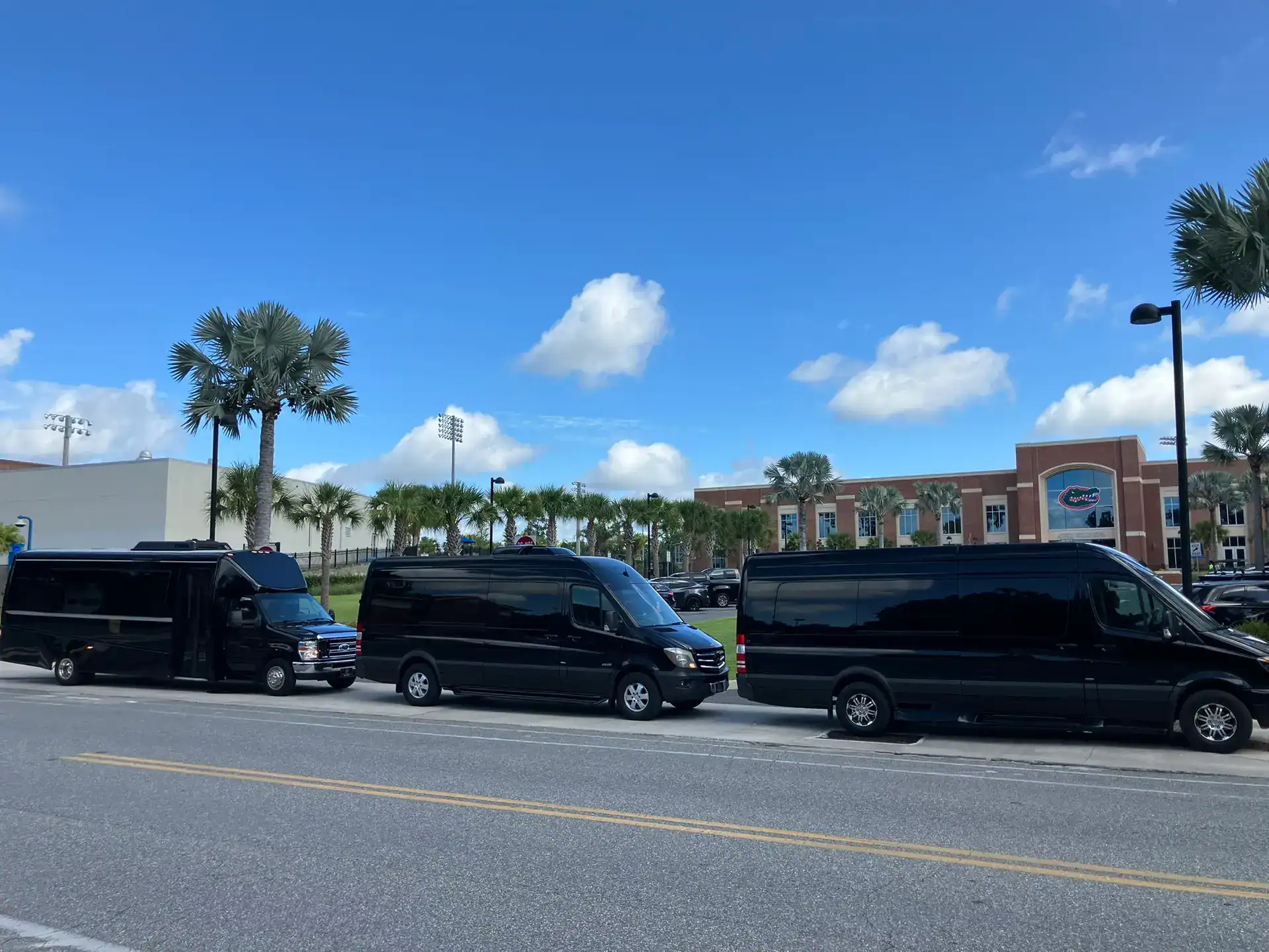 Luxury Mercedes Sprinter vans and an executive shuttle bus staged outside the Heavener Football Training Center at the University of Florida.
