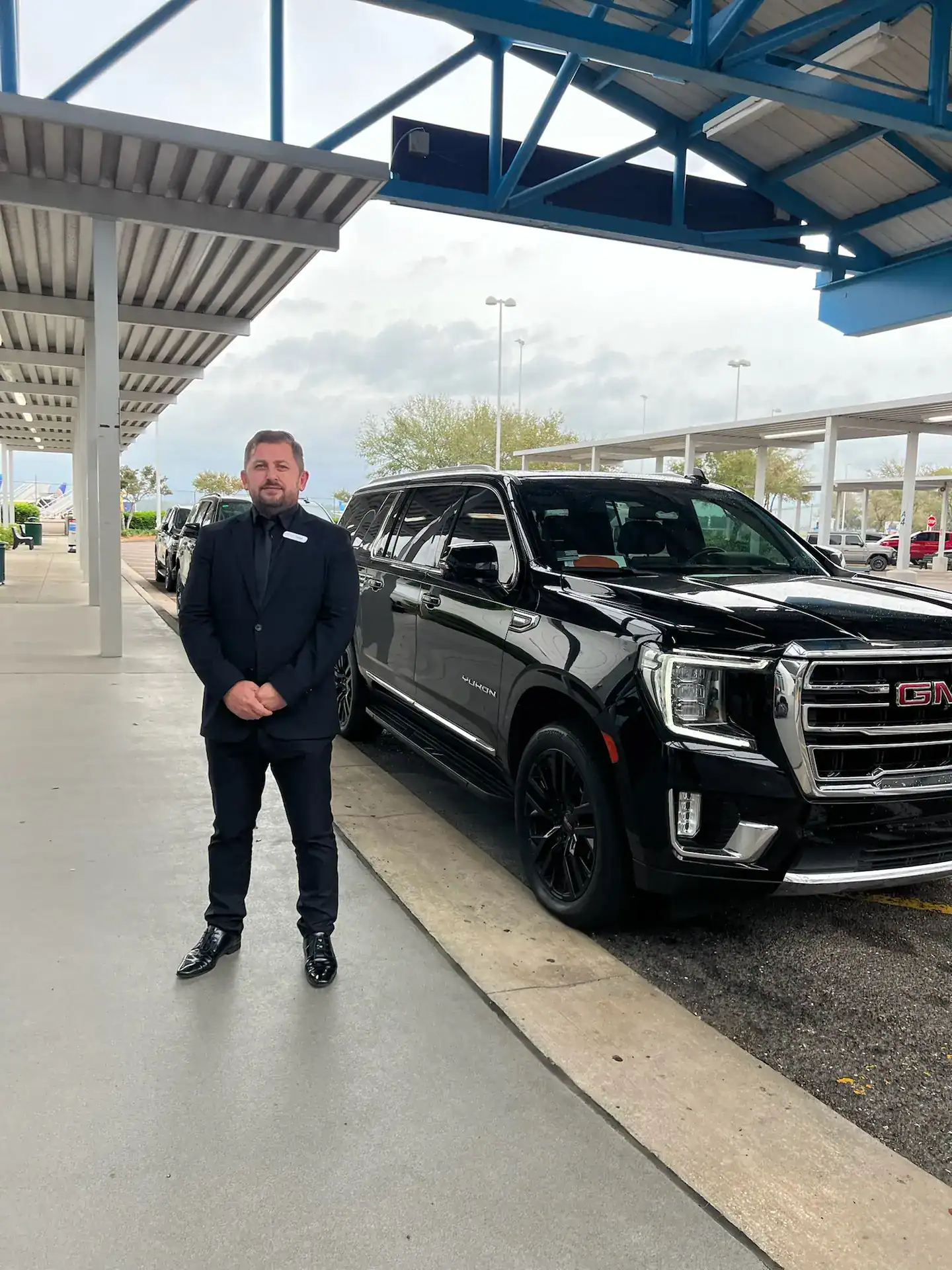 Professional chauffeur standing beside a luxury SUV in the ground transportation loading zone at Jacksonville International Airport.