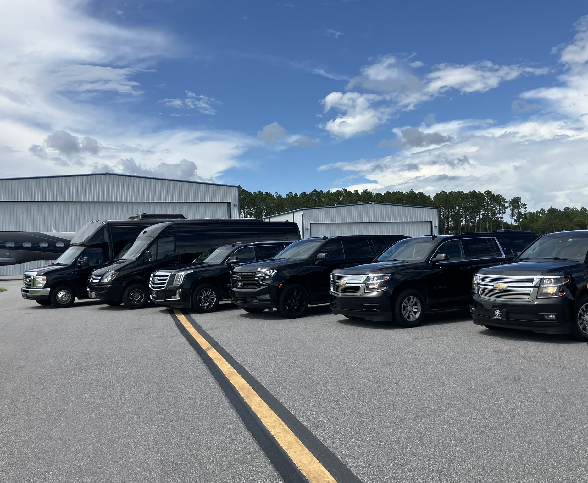 FTS Limousine lineup featuring Mercedes Sprinter, Cadillac Escalade, Chevrolet Suburban, and executive shuttle vehicles with a chauffeur outside the company's Gainesville, FL facility.