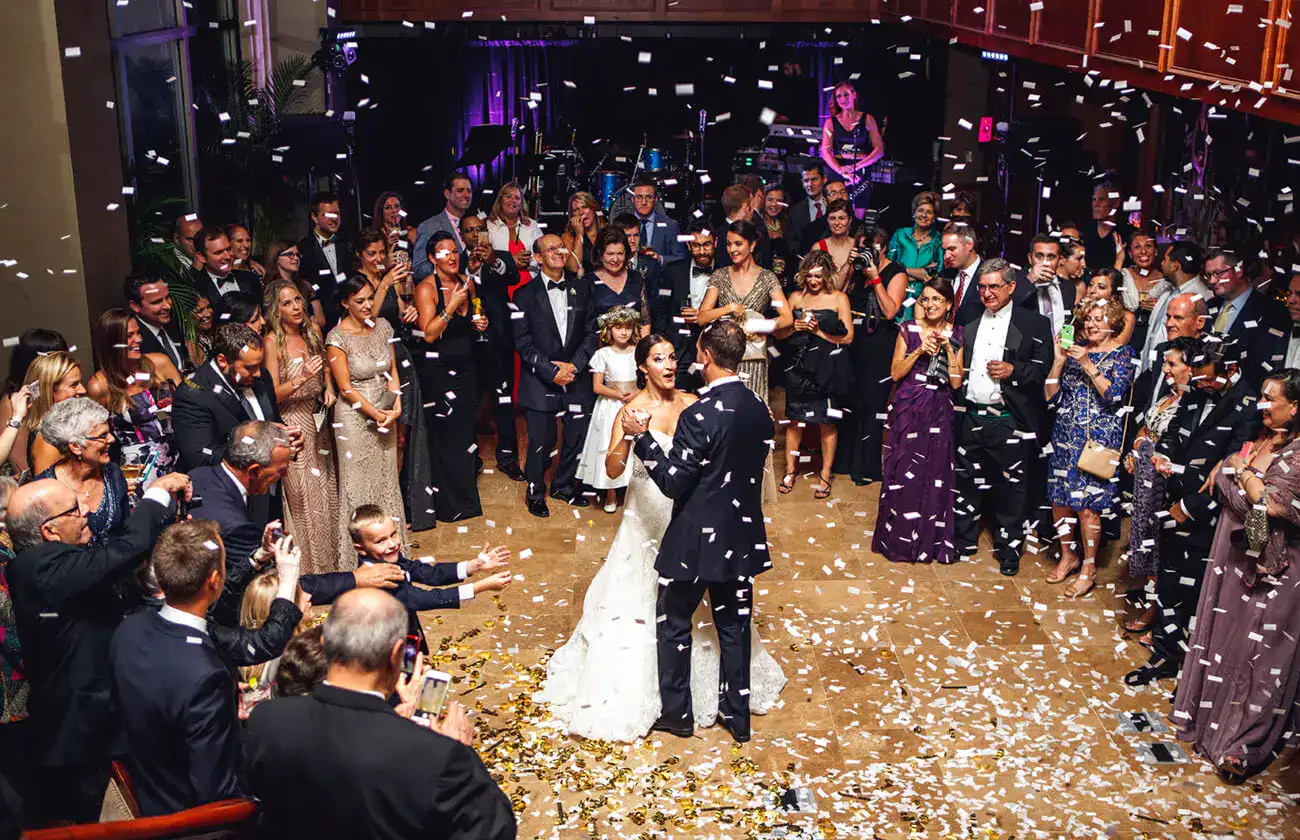 Bride and groom dancing together while wedding guests stand in a circle around them as confetti falls during the reception.