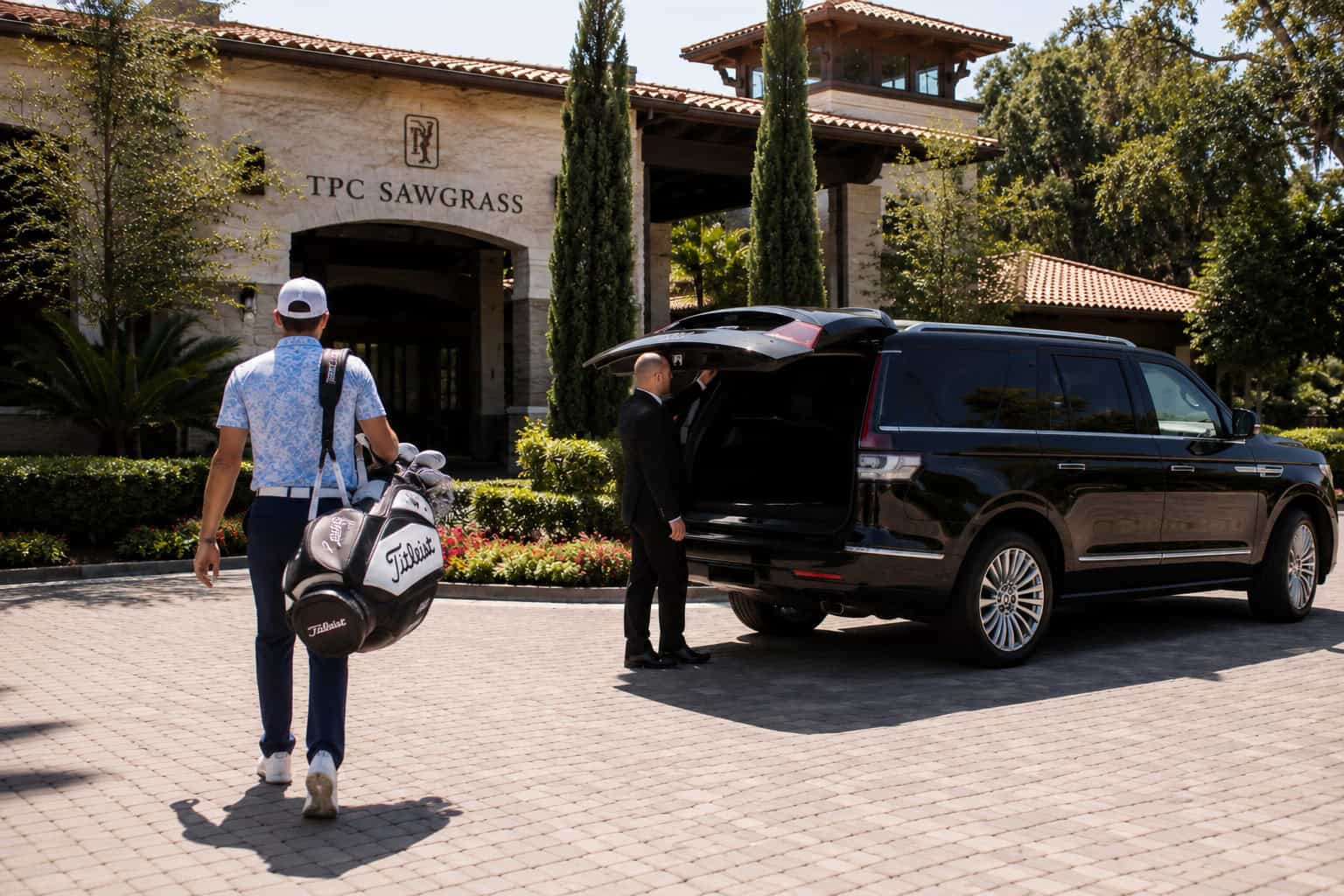 PGA TOUR golfer approaching the TPC Sawgrass Clubhouse where an FTS Limousine luxury SUV and chauffeur await.