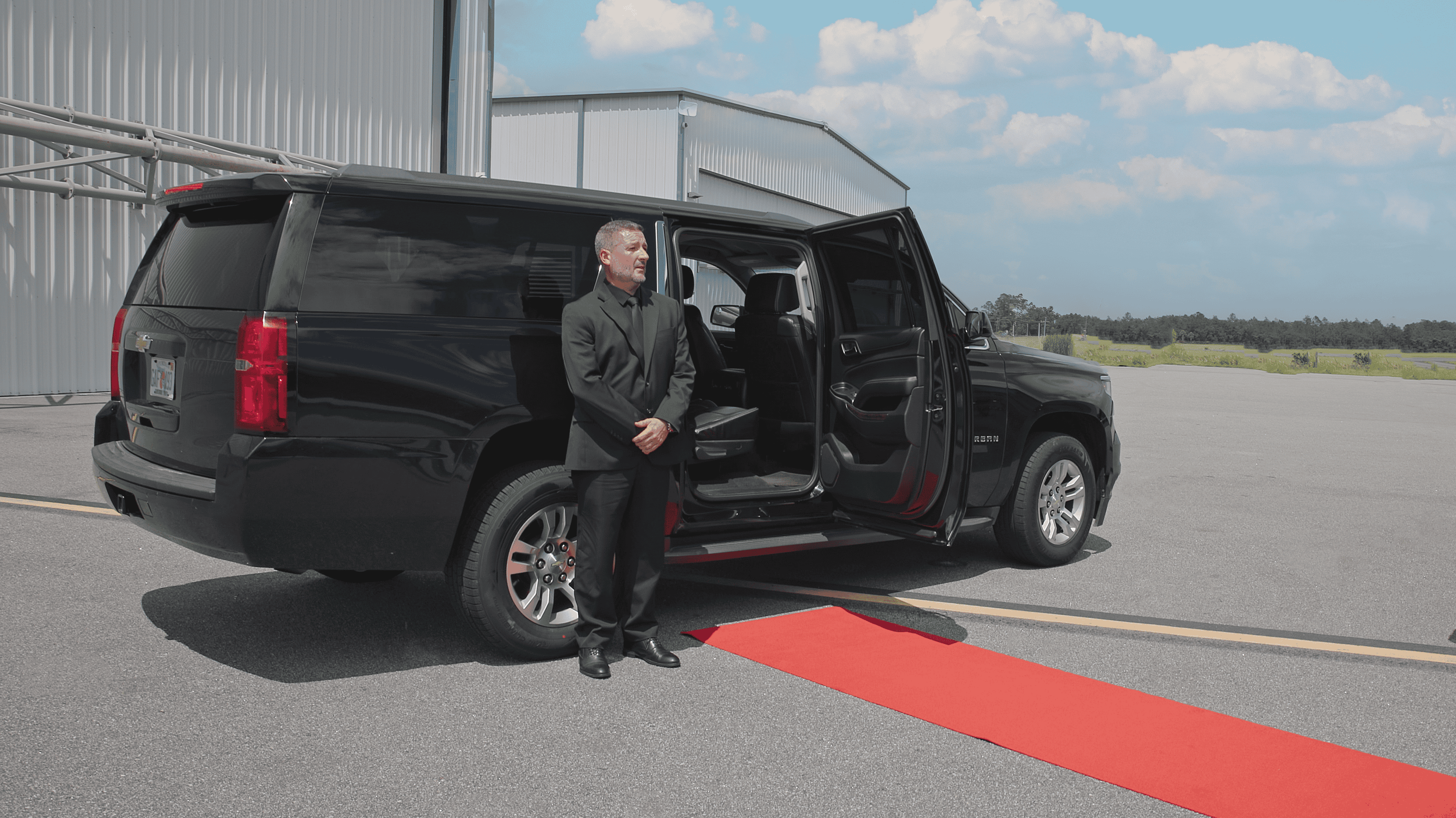 FTS Limousine chauffeur standing beside a luxury SUV with the rear door open and red carpet prepared for arriving private aviation passengers.